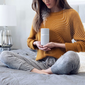 Foto ilustrativa de uma mulher sentada na cama inalando um aroma.